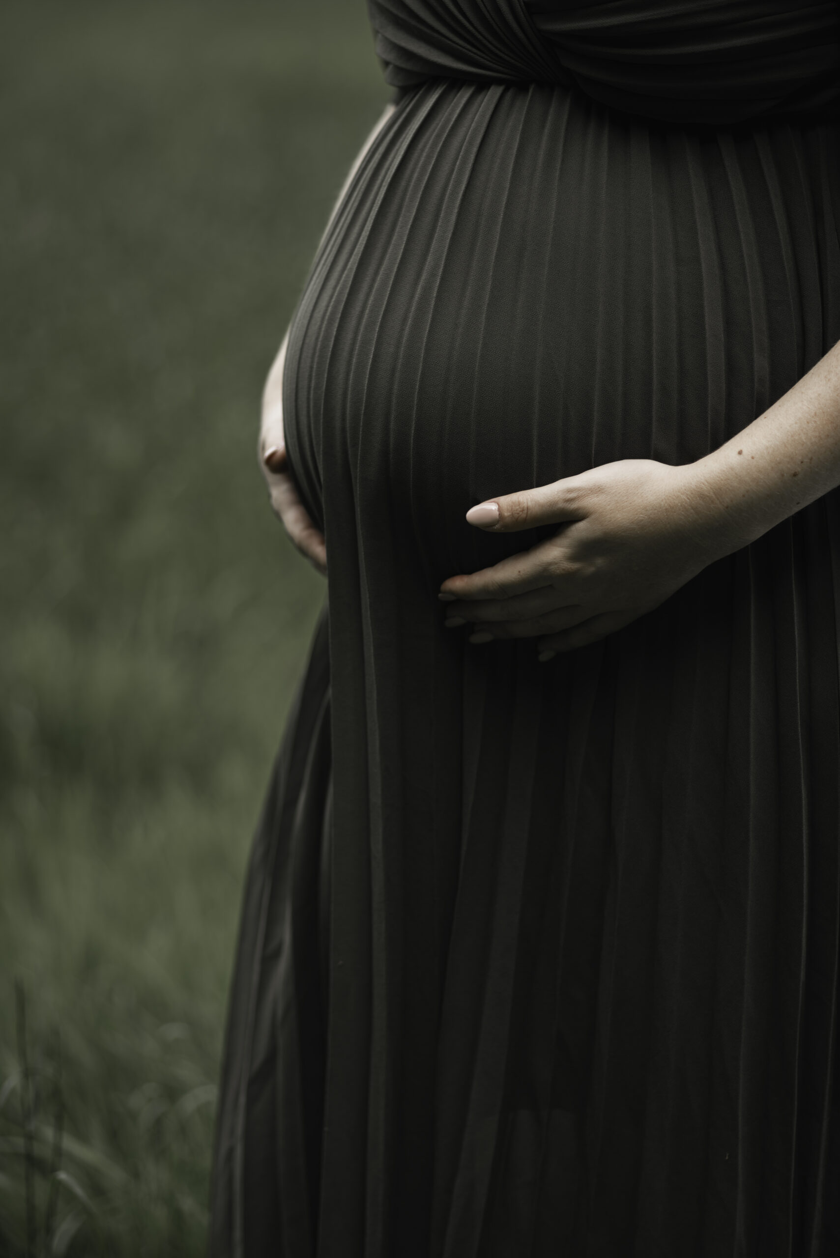 Stralende zwangere vrouw in een mooie groene plisse jurk die liefdevol haar buik vasthoudt
